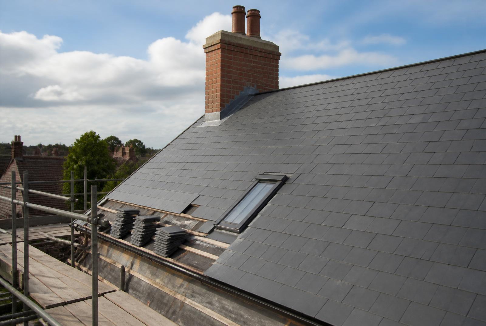 Pitched slate roof re-covering with scaffolding, lead flashing and new slate tiles on a period property, Dorset